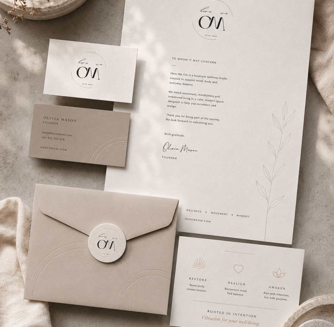 Here We Om wellness brand identity flat lay with logo card, letterhead, envelope, service card, and soft neutral stationery design.