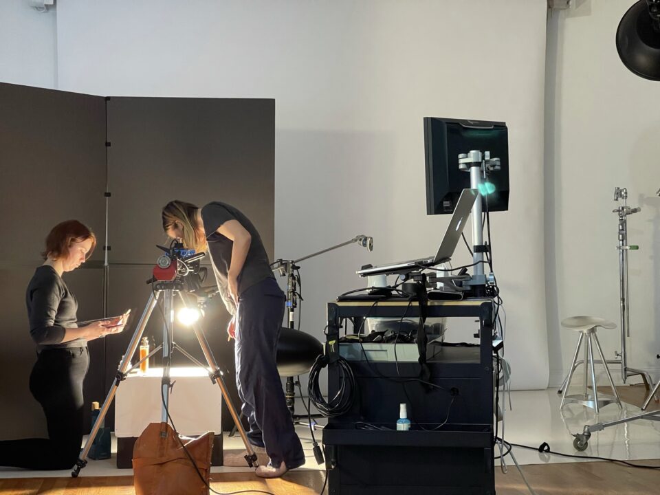 Professional photography workspace with camera, contact sheets, retouched image prints, lighting notes, and visual campaign references.