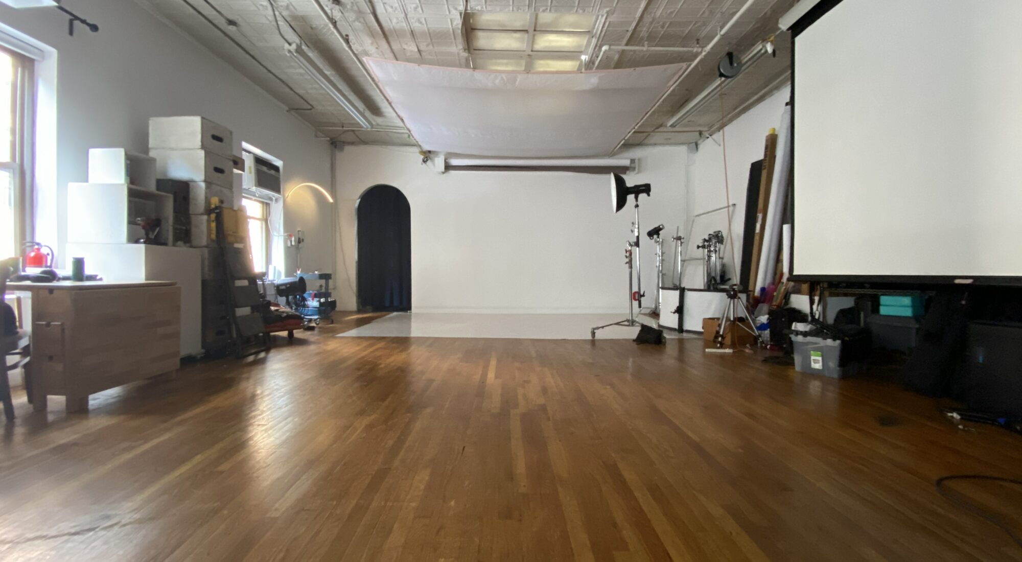 Spacious NYC photo studio rental with large windows, professional lighting equipment, seamless backdrop, makeup area, and open shooting space.